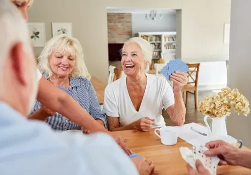 Three memory care patients laughing while playing card games to boost their memory